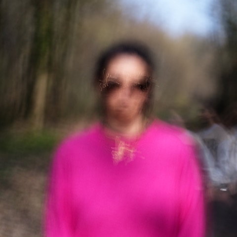 Portrait flou d'une femme en pull rose vif sur un chemin forestier