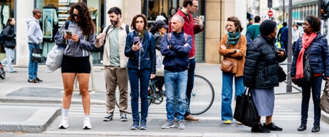 Rangée de piétons au bord du trottoir, l'une consulte son téléphone