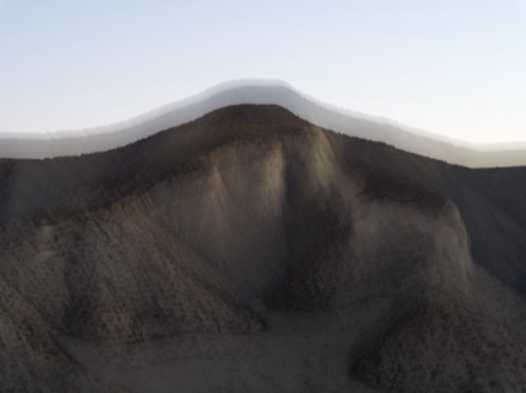 Colline sombre sous un ciel pâle, relief strié par le mouvement de l'appareil