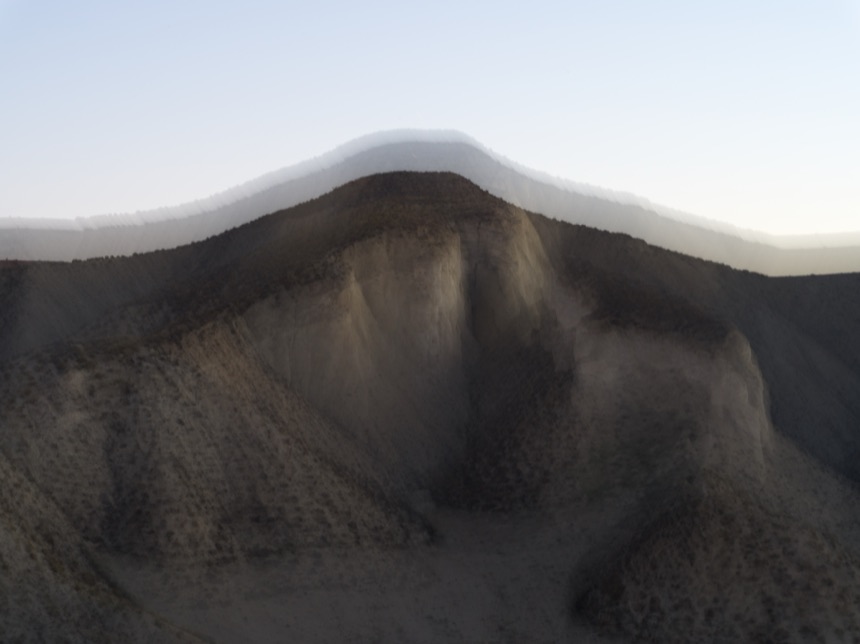 Colline sombre sous un ciel pâle, relief strié par le mouvement de l'appareil
